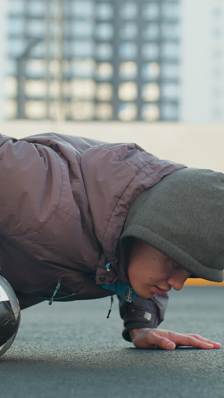 deportista realizando flexiones alternando la colocación de la mano en la pelota de fútbol mostrando fuerza, coordinación y agilidad en una arena deportiva urbana al aire libre con un fondo de edificio residencial moderno