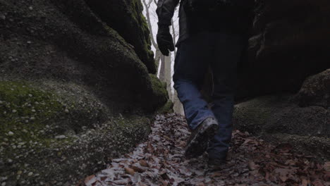 a hiker climbs between two rocky moss covered cliffs to scale the rock formation and ascend to the apex