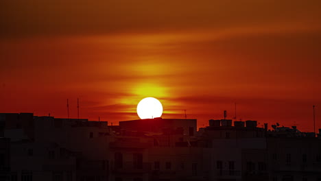 Timelapse-of-Gzira,-Malta-of-a-spectacular-sunrise,-passing-through-clouds-and-appearing-to-distort-as-it-rises-over-many-apartment-buildings