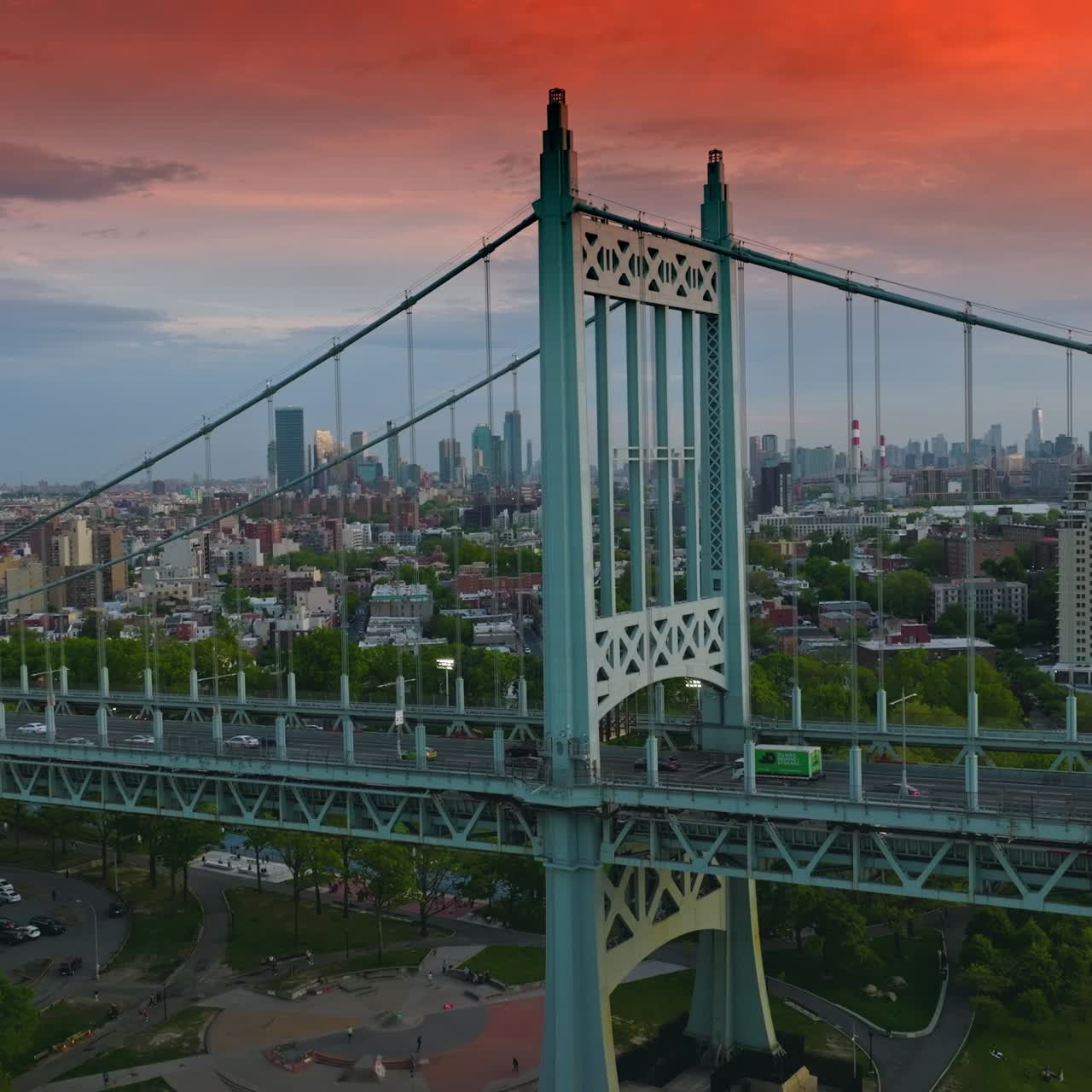 Robert F. Kennedy Bridge with parking lot and recreational area under. Triborough bridge at the backdrop of city buildings under pink sky