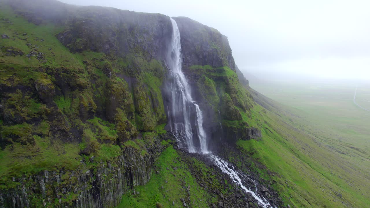 cascada escénica que desemboca en acantilados de montaña musgosos y rocosos en un día brumoso
