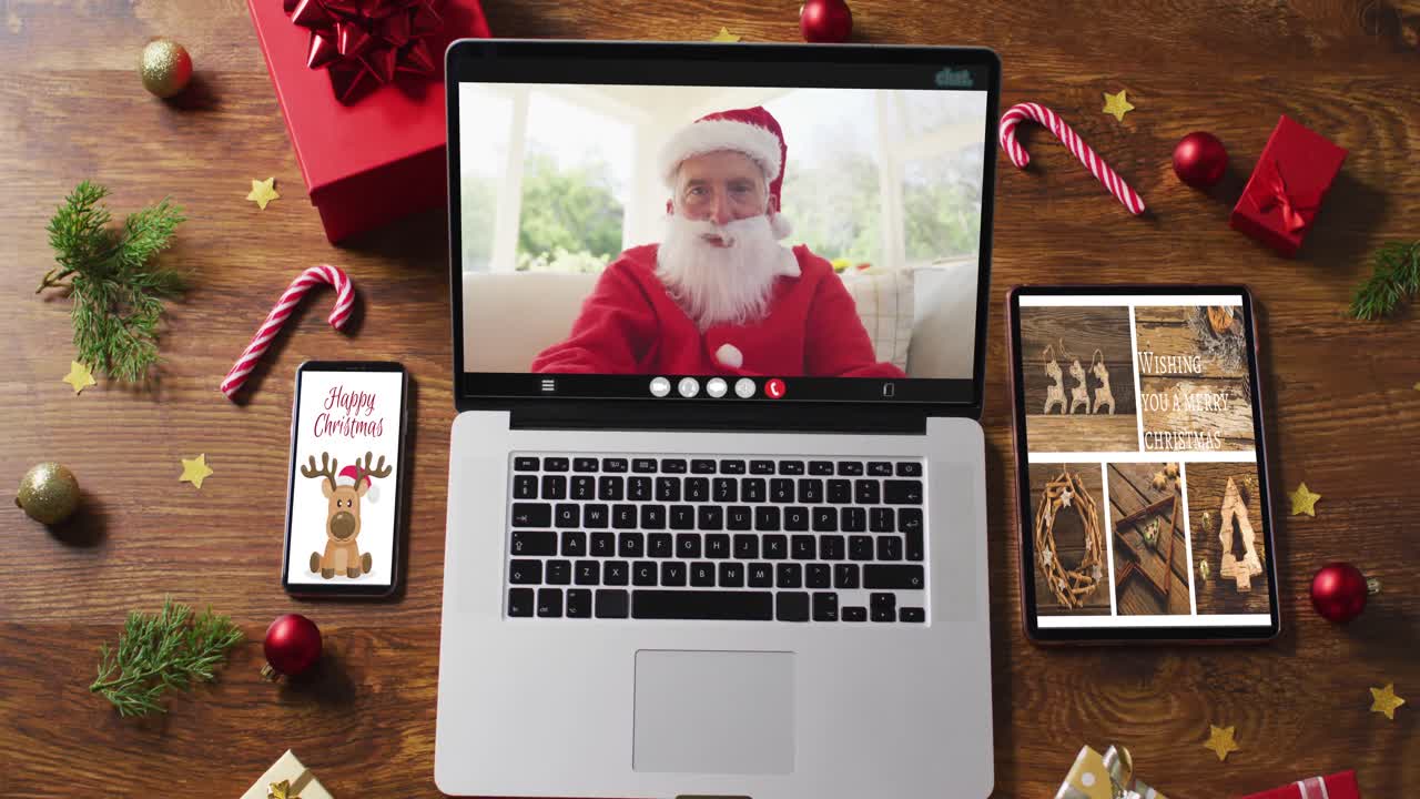 feliz senior caucásico santa en videollamada en computadora portátil, con teléfono inteligente, tableta decoraciones de navidad