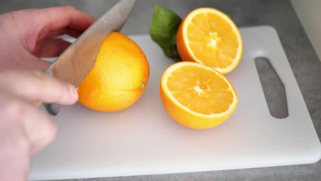 mano masculina corta una naranja por la mitad con un cuchillo en una tabla de cortar