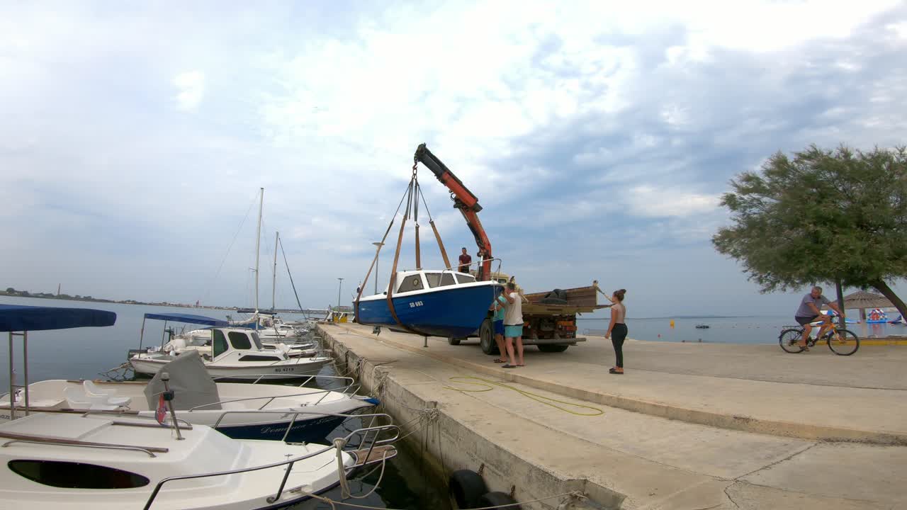 A blue boat being lifted by a crane at a dock in a marina