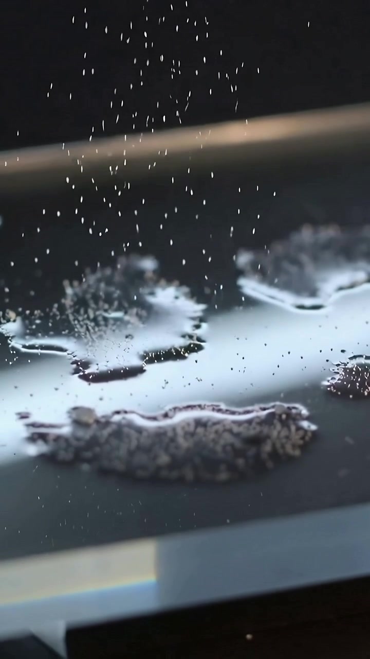Video verticale: Granuli che cadono su piccole pozze di liquido su una piastra metallica sul fornello