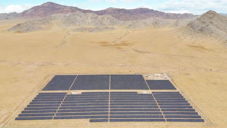 aerial view of hundreds of solar panels in the uliastai desert, mongolia. the drone reveals the plant's vast scale in the remote, barren landscape, with mountains visible in the background.