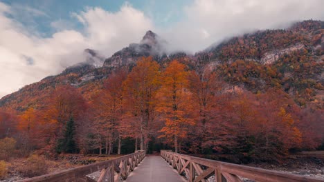 vista frontal del puente que cruza el río en la entrada del parque nacional de ordesa durante la temporada de otoño otoño con hermosos colores de árboles picos nevados y excursionistas