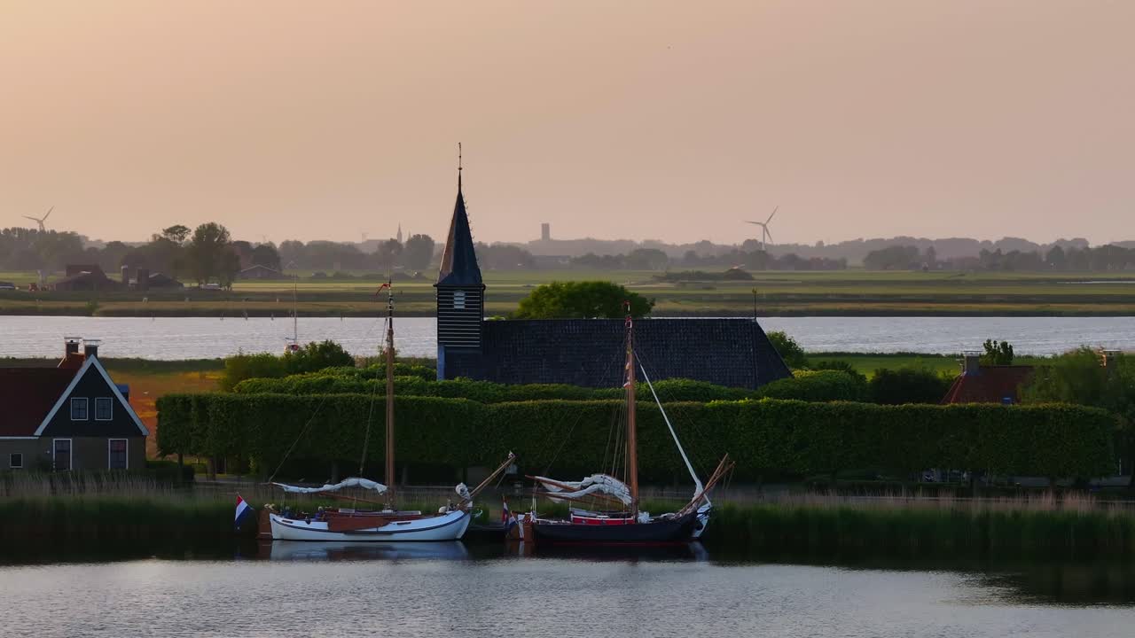 Luftaufnahme einer Kirche und eines Segelboots auf dem ruhigen See während eines wunderschönen Sonnenuntergangs in Sandfirden, Friesland.