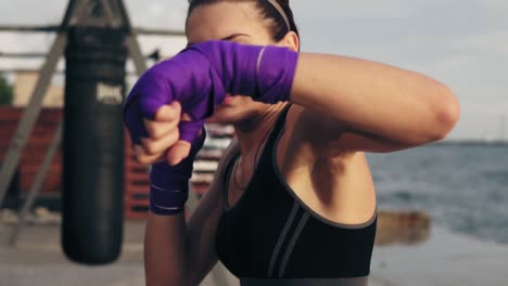 close up view of a young woman shadowboxing with her hands wrapped in purple boxing tapes looking in the camera. beautiful