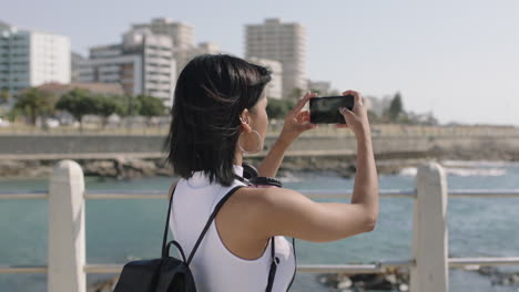 retrato de una joven mujer hispana tomando una foto de la vista de la costa usando un teléfono