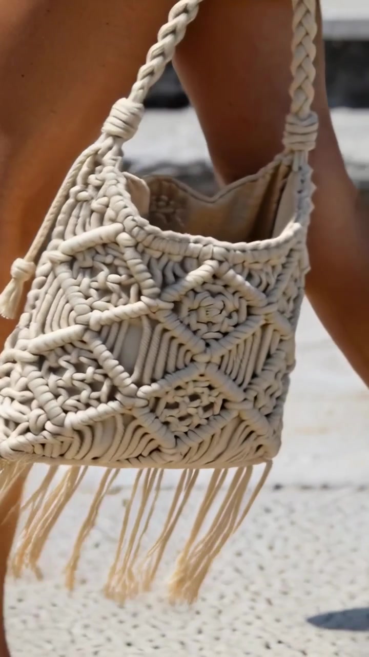 Video vertical: Mujer caminando por una pasarela pavimentada, llevando un bolso de macramé con flecos, en traje de baño