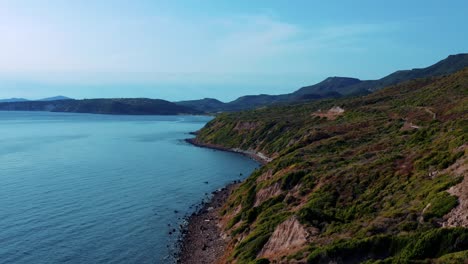 Drone view of rugged green hills meeting calm blue waters of Andaman Sea along peaceful southern Thailand coast, under clear sky with distant mountains in background