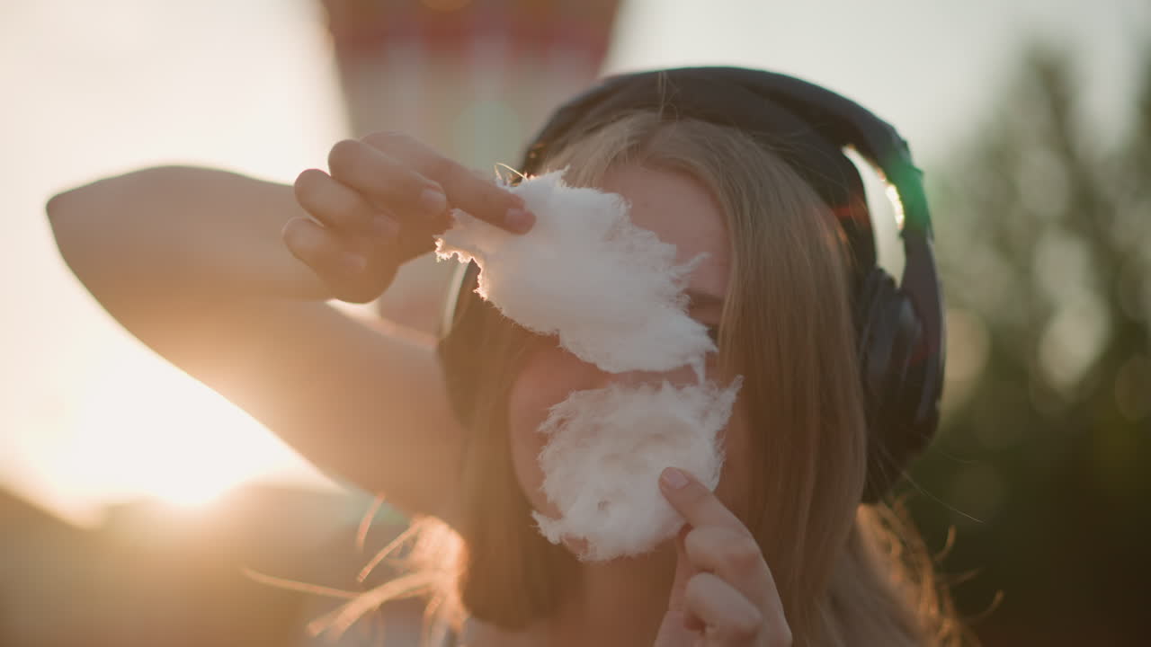 Legende portræt med slik, nærbillede af kvinde, der laver candyflossfigurer under solnedgangsfestival, intimt festivalbillede, der indfanger kvinde, der laver legende candyflossfigurer mod solnedgangens glød