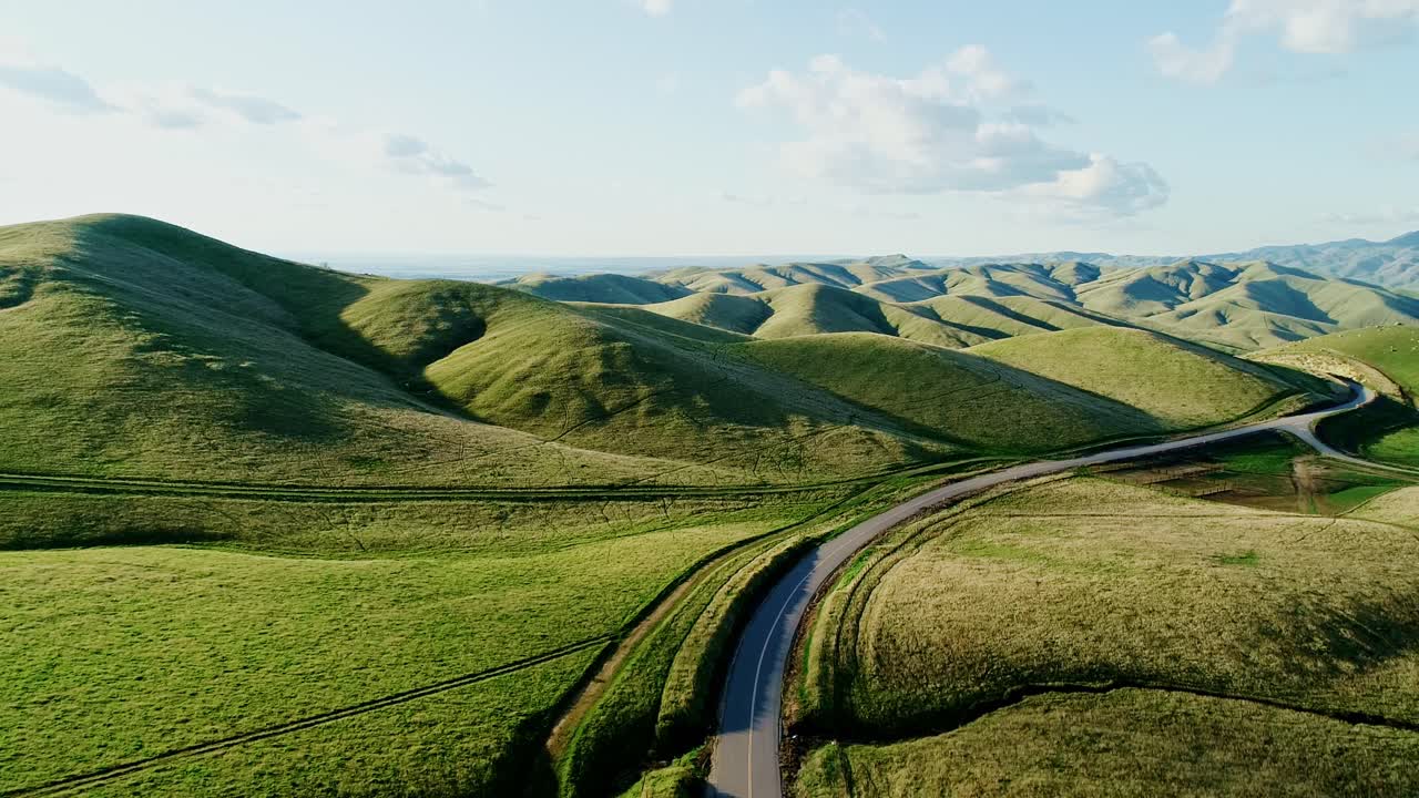 Serene aerial view of sunlit fields and rolling hills with peaceful winding road