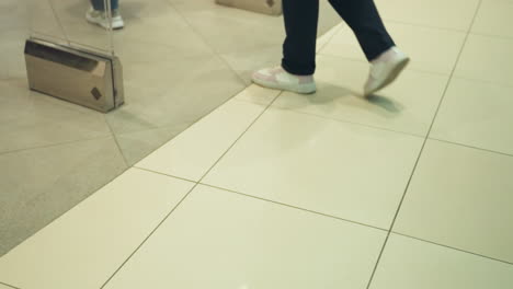 a close-up view of people s feet moving in a shopping mall, showcasing the lower part of the body and footwear. shot from the first person perspective with a handheld camera