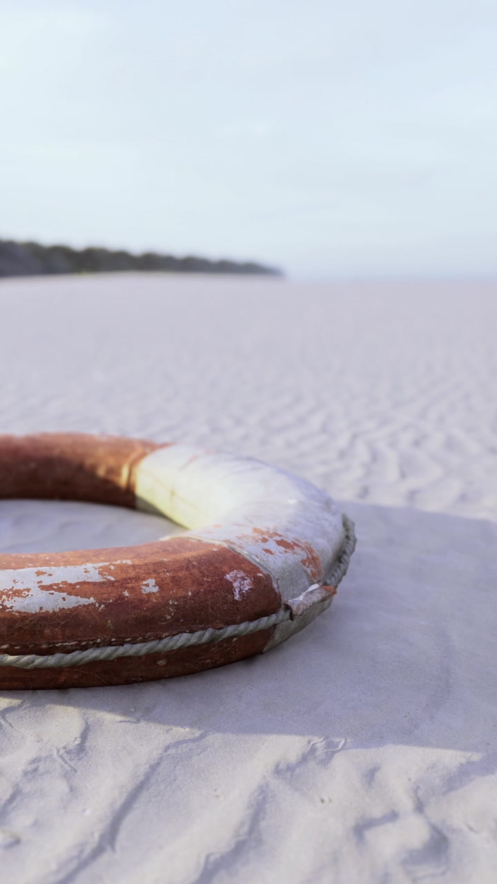 Redningskrans på sandstrand med fjern kystlinje i dagslys.