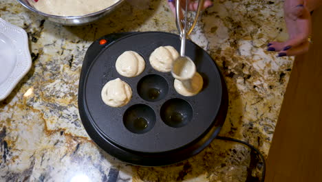 batter for ebelskivers being put in a dutch oven with a blackberry in the center