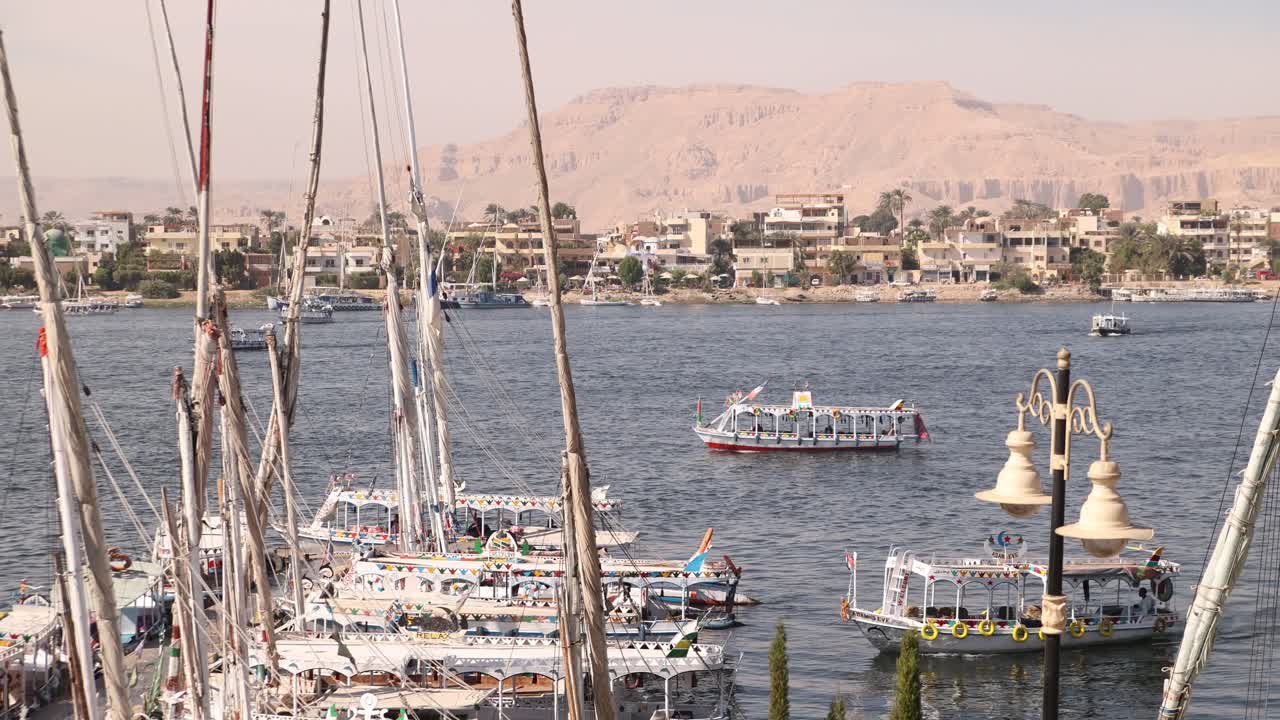 panorámica de barcos flotando a lo largo del nilo con montañas en el fondo y barcos de vela en el primer plano en luxor, egipto