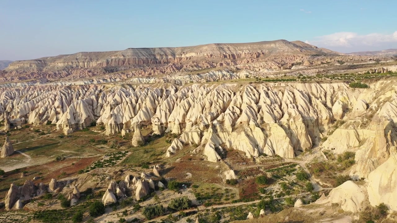 Vista panoramica aerea con drone di formazioni rocciose bianche, camini delle fate conici e montagne di tufo dalla cima piatta nella Valle delle Rose, Cappadocia, Nevsehir, Turchia, sotto un cielo azzurro e limpido.