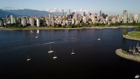 flying over the kitsilano beach, kits beach with white sailboats on the blue ocean with downtown skyline, skyscrapers and english bay in vancouver, british columbia, canada