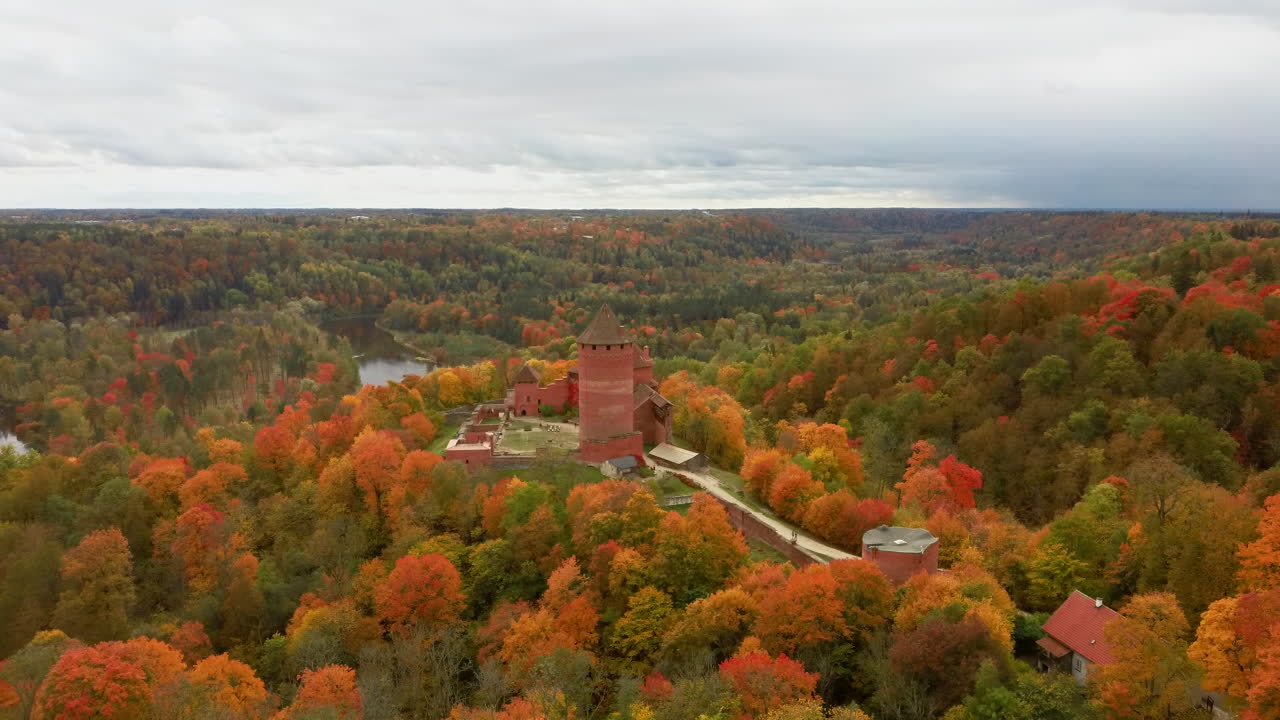 vista aérea del paisaje otoñal del antiguo castillo de turaida, rodeado de bosques de colores amarillo brillante, naranja y árboles verdes, día soleado