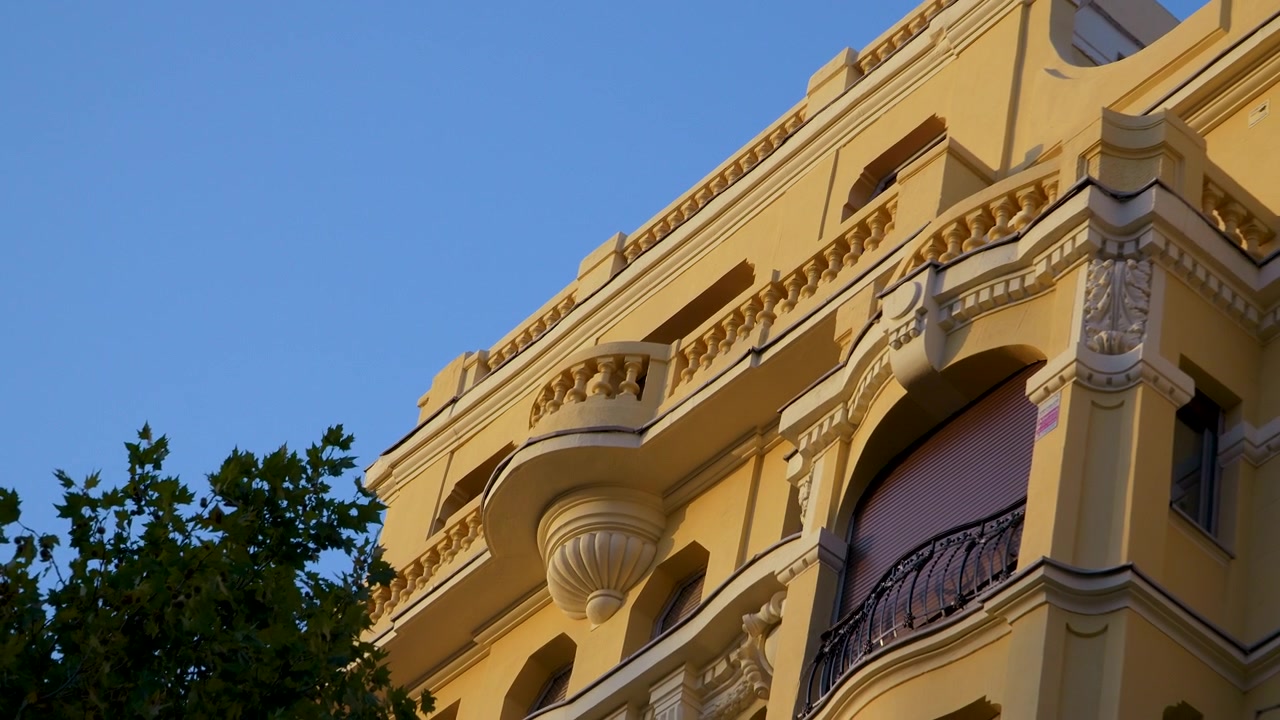 Un'inquadratura dal basso di un classico edificio spagnolo giallo a Madrid, con intricati dettagli architettonici e balconi in pietra, contro un cielo azzurro limpido