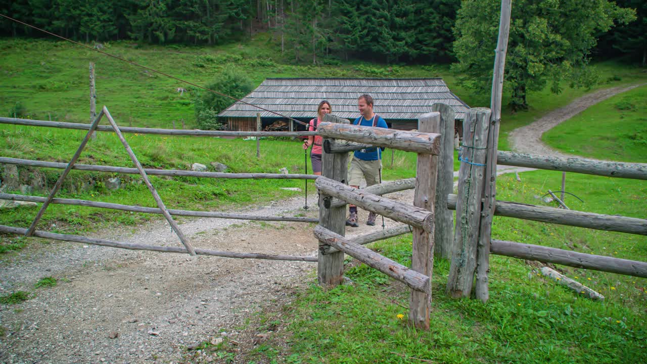 Excursionistas caminando hacia una puerta de madera y abriéndola, bosque y casa al fondo
