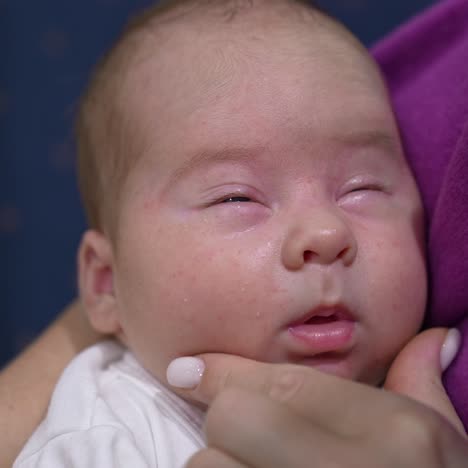 face of an infant baby sleeping deeply and doesn't want to wake up. loving mum trying to wake her kid up and touches his sweet cheeks tenderly. close up