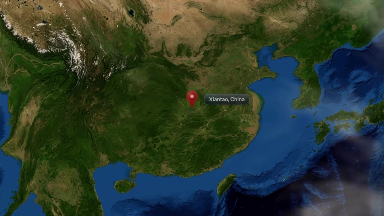 Satellite camera zooms from space into Asia, pinpointing Xiantao, China with a location marker. Includes NASA public domain imagery.