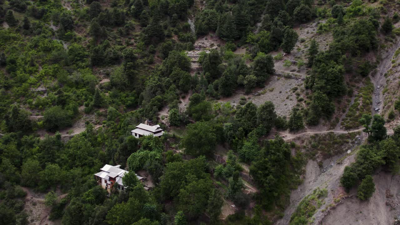 Isolated houses nestled on a forested Himalayan hillside near a landslide-prone area