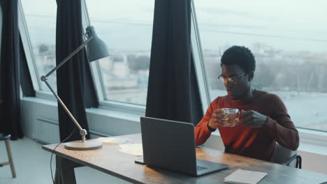 Black-Man-Using-Laptop-and-Drinking-Tea-in-Rooftop-Office