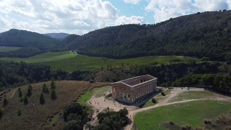 wide aerial of a greek temple with lush green forests and rolling landscape