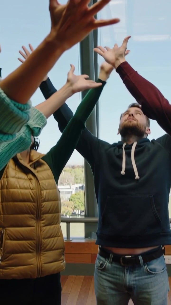 Vertical video: Raising two adults in tan-vest navy-hoodie lifting arms up on cue at atrium windows