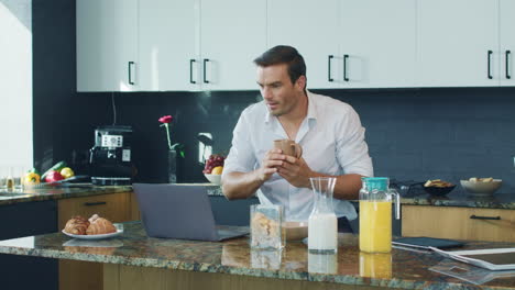 Smiling-man-watching-video-standing-in-kitchen.-Happy-person-scrolling-computer.