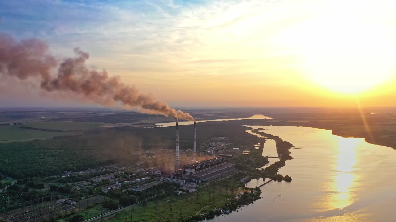 Smoke from pipes on factory near the river at sunset. Air pollution from industrial plant on the natural background in the evening.
