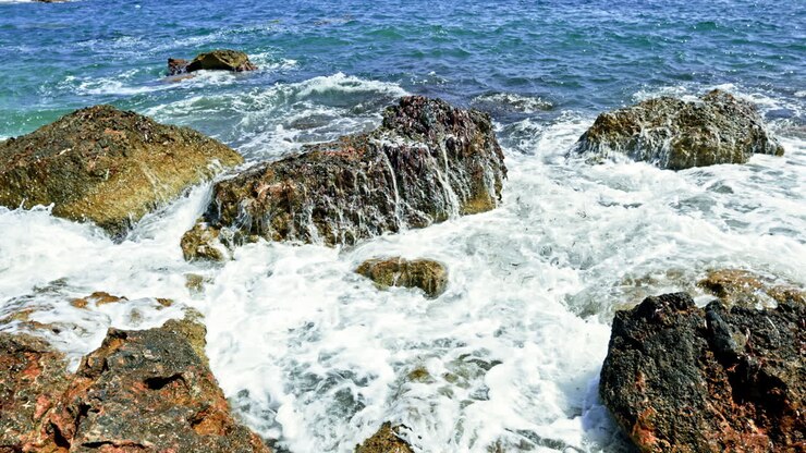 Costa oceanica rocciosa. Grandi onde che si infrangono contro le rocce sullo sfondo dell'oceano blu. Onde marine che si infrangono contro le rocce formando schiuma di mare