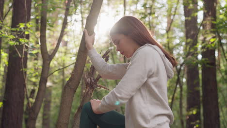 young woman stretches bending leg after jogging in park. lady performing stretching exercises to relax muscles after running in nature. relaxation after workout