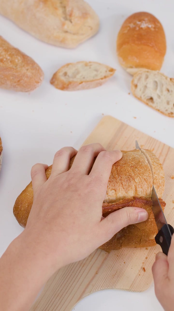 Close-up overhead shot of hands slicing crusty bread on a wooden board with bright lighting.