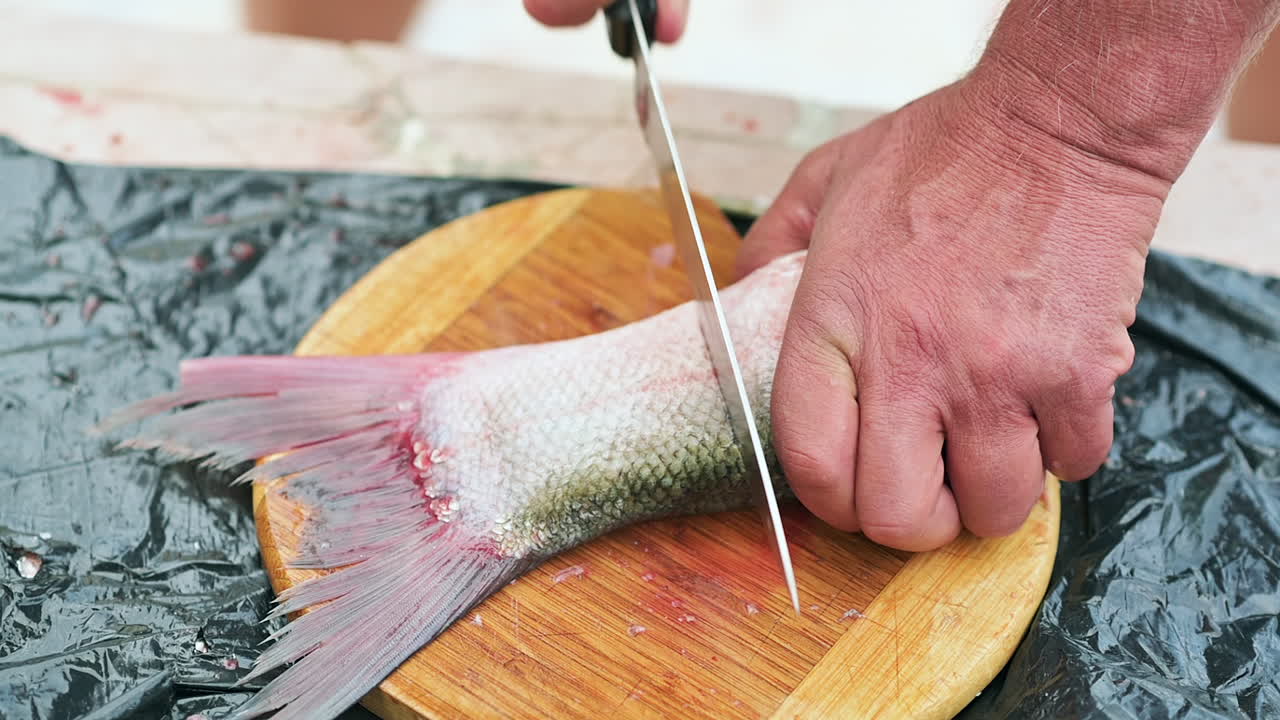 Close up of a man slicing a fish tail on a wooden cutting board