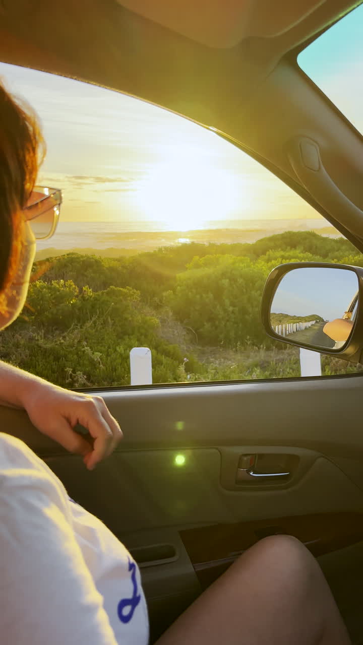 Donna sul sedile del passeggero con il finestrino aperto si gode un vivace tramonto durante un giro in auto. Verticale.