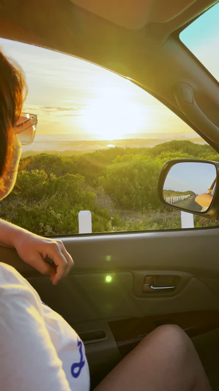 Donna sul sedile del passeggero con il finestrino aperto si gode un vivace tramonto durante un giro in auto. Verticale.