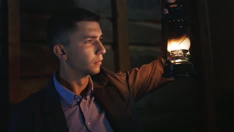 scared young man in a dark hallway holding an oil lamp in his hand dressed in a suit