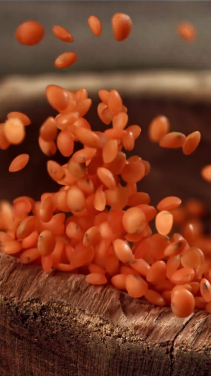 Red Lentils Falling into a Rustic Wooden Bowl in Slow Motion