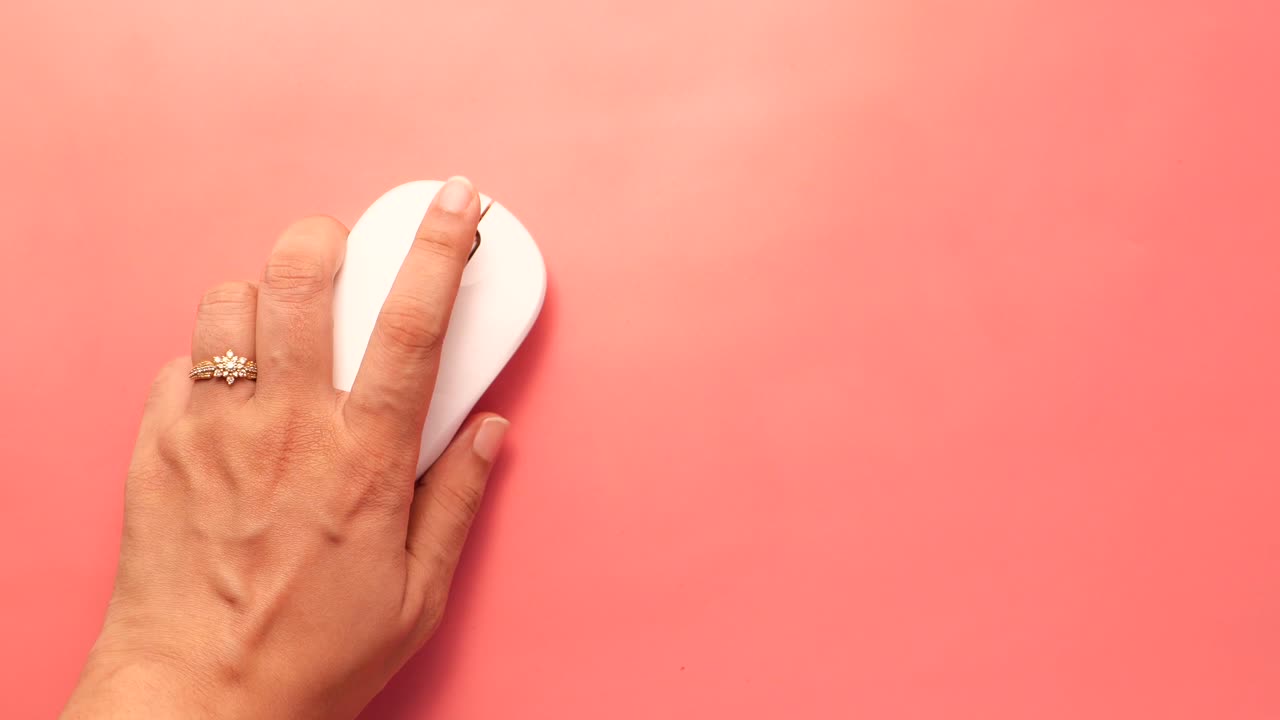 mano sosteniendo un ratón de computadora blanco en una superficie rosa