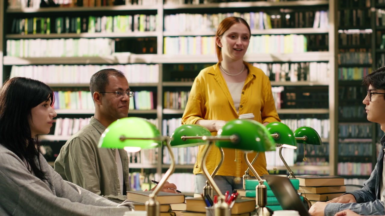 Mentor at group study speaking with peers seated at library table