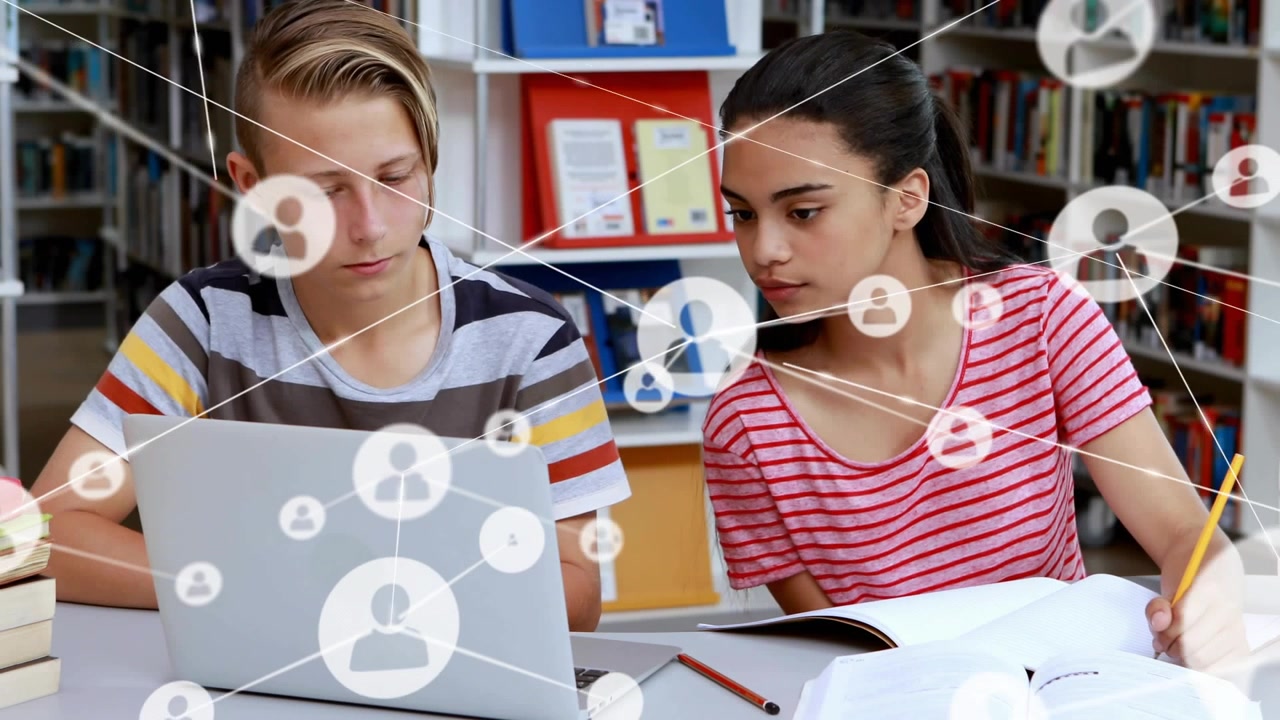 Teen students taking notes in library watching user icon appearing above laptop building network