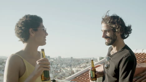 cheerful couple dancing and toasting with beers at rooftop party