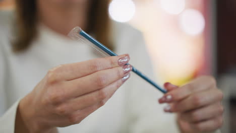 close-up of hands with painted nails carefully examining a straw wrapped in transparent plastic, set in a modern indoor environment with soft lighting and a blurred vibrant background