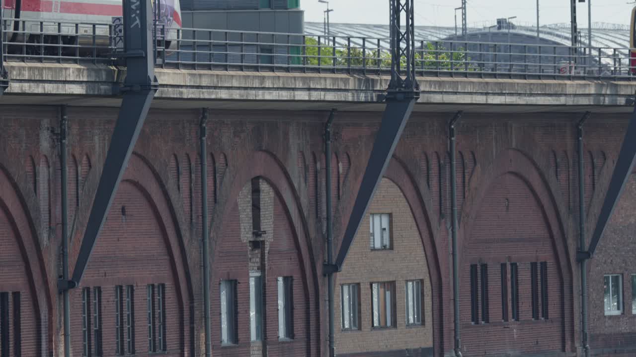 Modern passenger train moves across elevated brick railway bridge in daylight, urban cityscape background