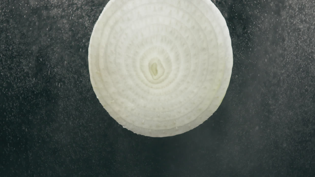 ломтик лука, обрызганный сильным туманом из капель воды с жидкостью в замедленной съемке на черном фоне с подсветкой